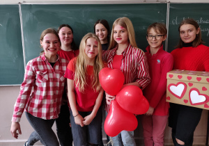 Grupa uczniów w czerwonych strojach z balonami i pudełkiem w serduszka.