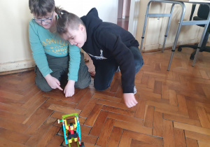 Dwóch uczniów siedzi na podłodze i sprawdza zbudowany model.