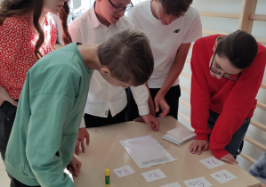 Grupa uczniów rozwiązuje zadanie przy stoliku szkolnym.