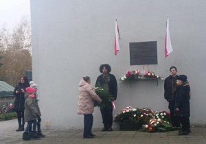Pani wicedyrektor składa kwiaty pod tablicą pamiątkową.