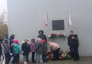 Uczniowie klas młodszych przy tablicy pamiątkowej.