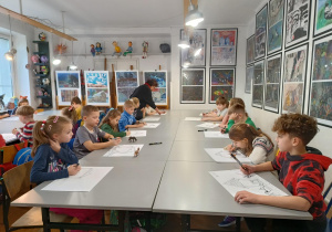 Grupa uczniów z 2 A rysuje czarnymi mazakami pod okiem pani Bogusi.