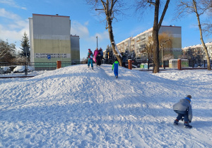 Grupa uczniów wspina się na ośnieżoną górkę