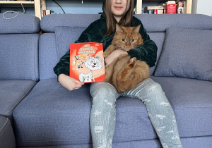 Dziewczynka z książką w ręku siedzi na sofie.