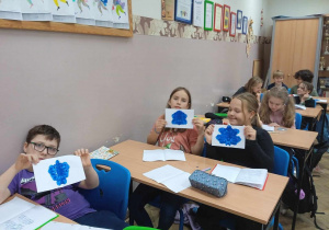 Grupa dzieci w ławkach prezentuje swoje prace.