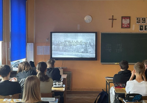 Uczniowie siedzą w ławkach i oglądają film.