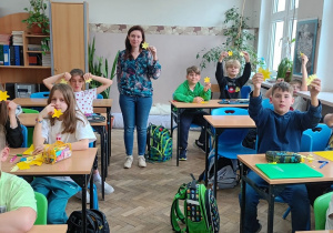 Uczniowie w ławkach z papierowymi żonkilami w rękach.