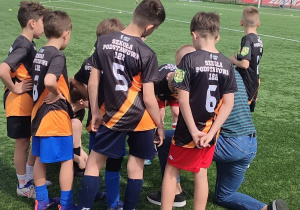 Grupa uczniów w strojach sportowych stoi w kole.