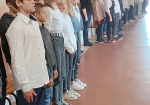 Uczniowie stoją na baczność na korytarzu szkolnym
