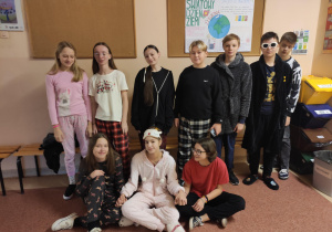 Grupa dzieci w piżamach na korytarzu szkolnym.