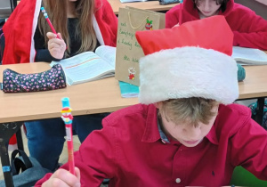 Uczniowie w klasie w czapkach Mikołaja z długopisami w rękach.